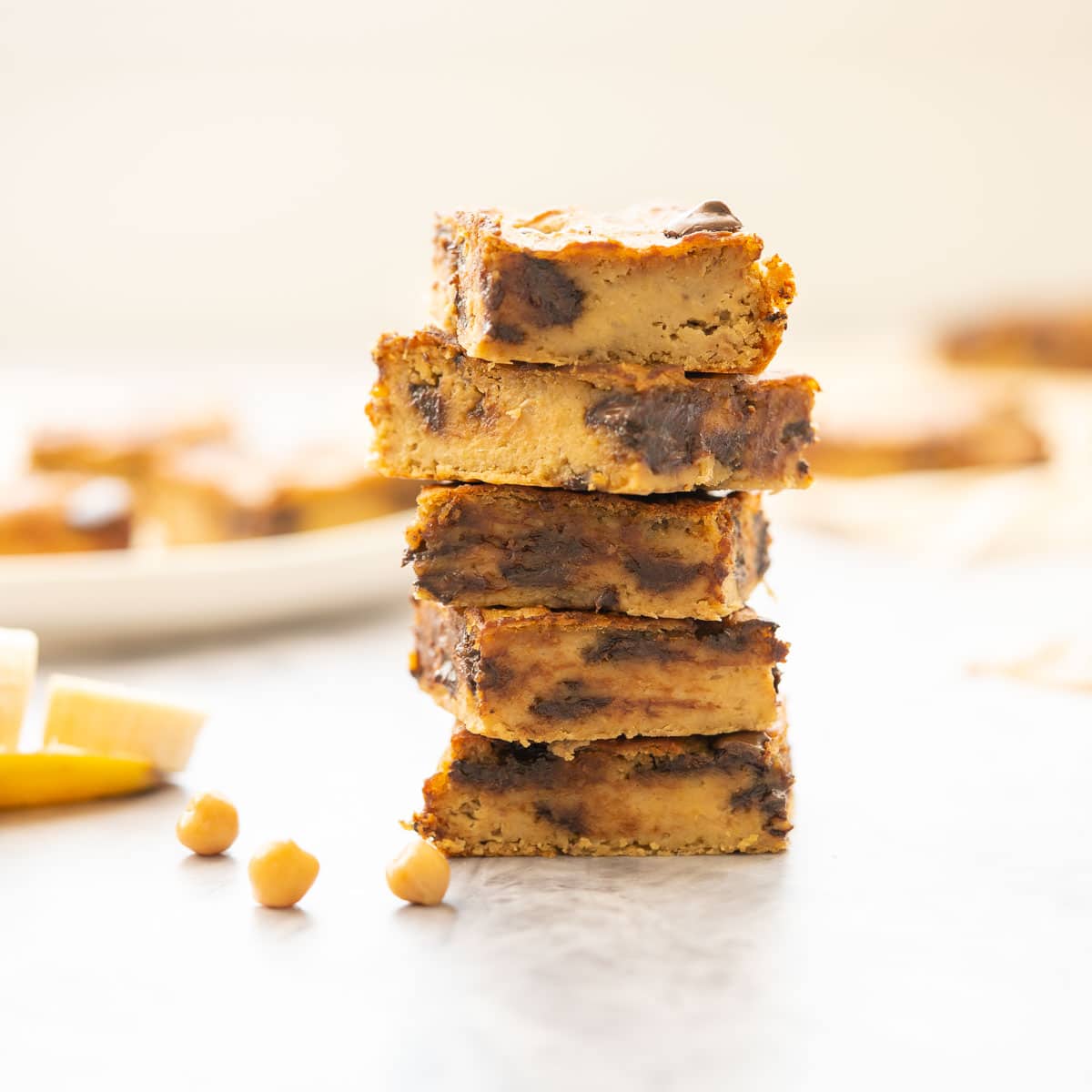 stacked pieces of sliced chickpea blondie sitting on the bench with a sliced banana and chickpeas scatted next to it