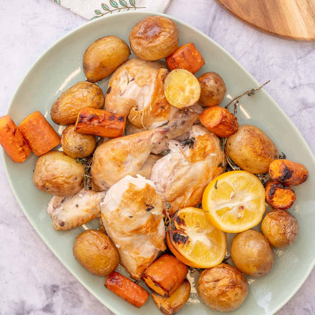 A large mint green serving dish filled with roasted potatoes, carrots and chicken sitting on the bench in front of the crockpot 
