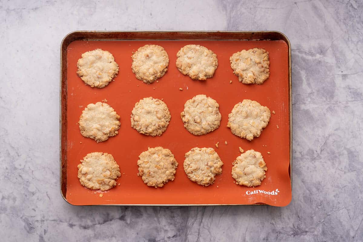 Lined tray with 12 baked golden brown Gluten Free Coconut Cookies sitting on a marble bench