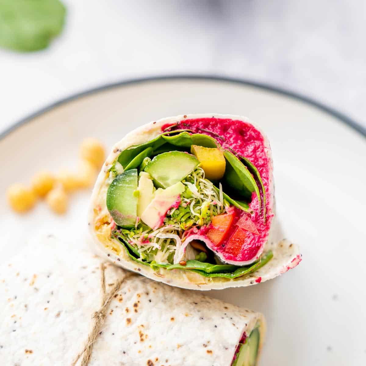 Halved filled wrap stuffed with beetroot hummus, cucumber, sprouts, spinach and capsicum sitting on a dish on a bench