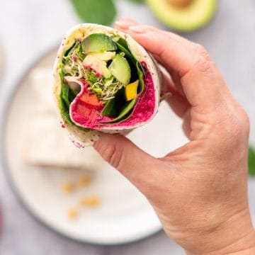 A wrap filled with colourful veggies being held up to the camera.