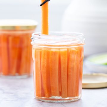 A carrot baton being lifted from a jar of pickled carrots with chop sticks.
