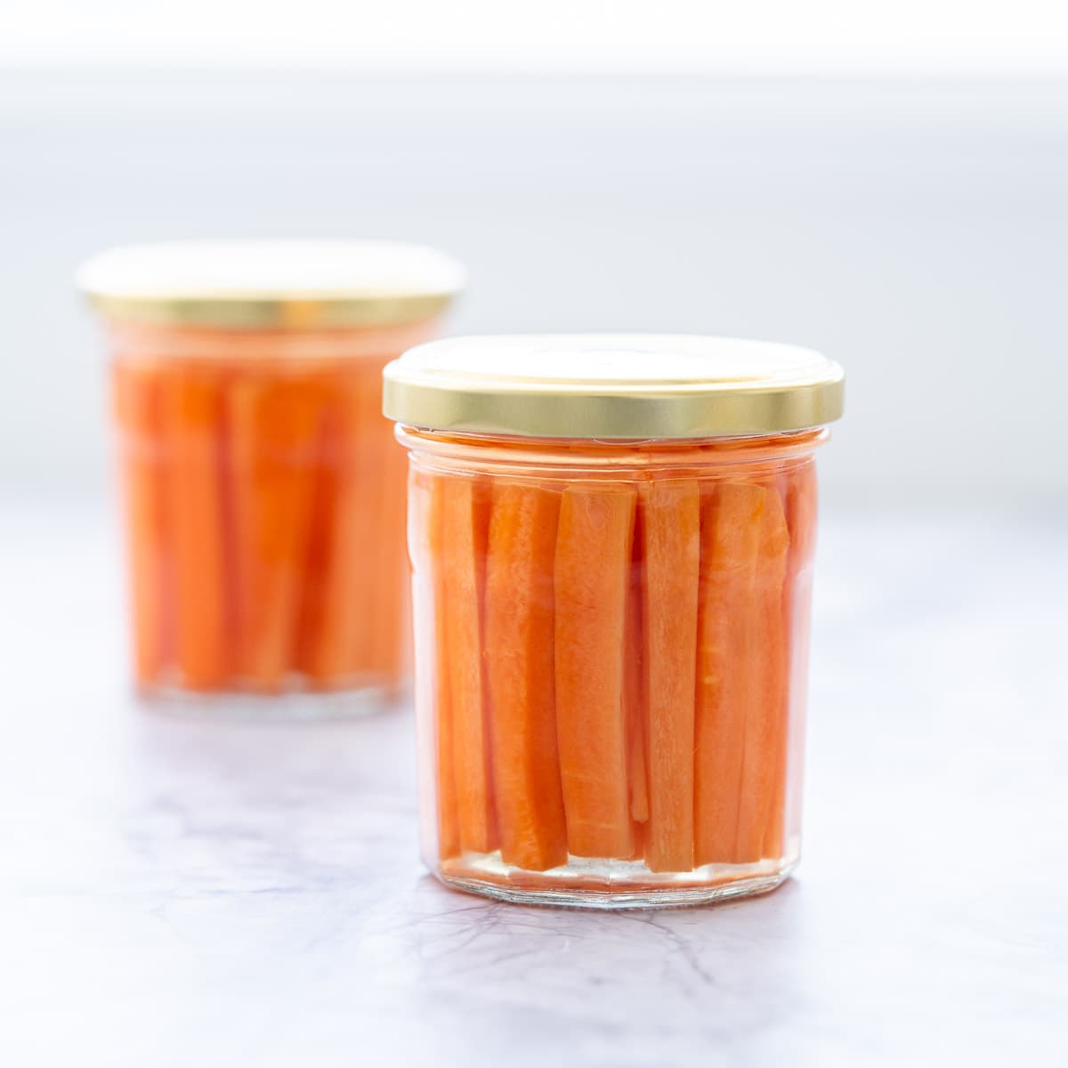 2 glass  jars full of pickled battened carrots sitting on a bench