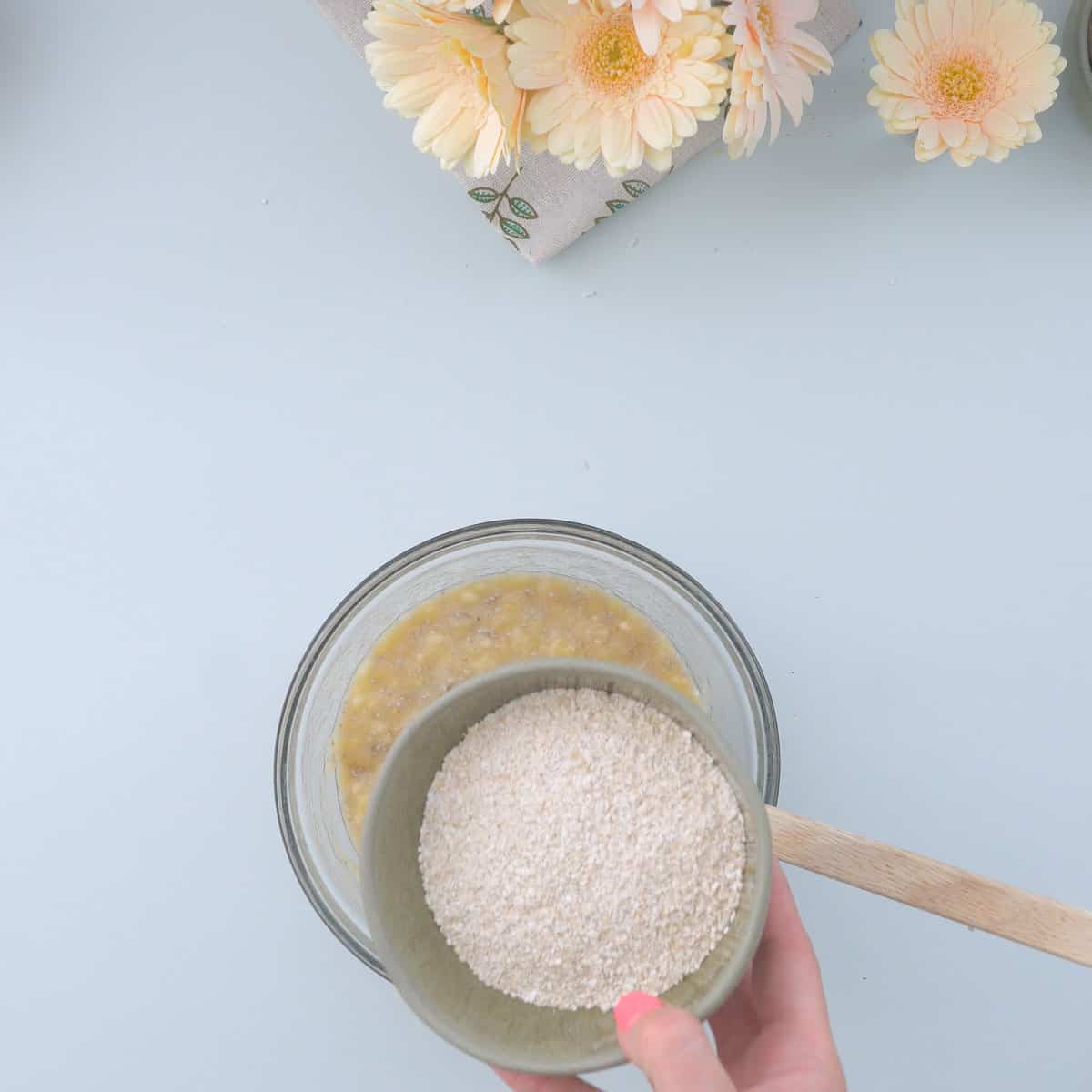A bowl of oat flour being added to a bowl of wet ingredients.