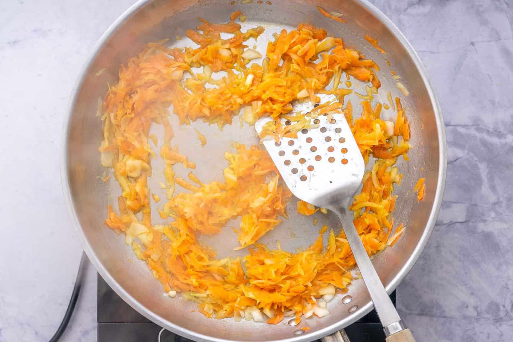 a frypan full of sautéed onion and carrot with a spatula resting on the side. 