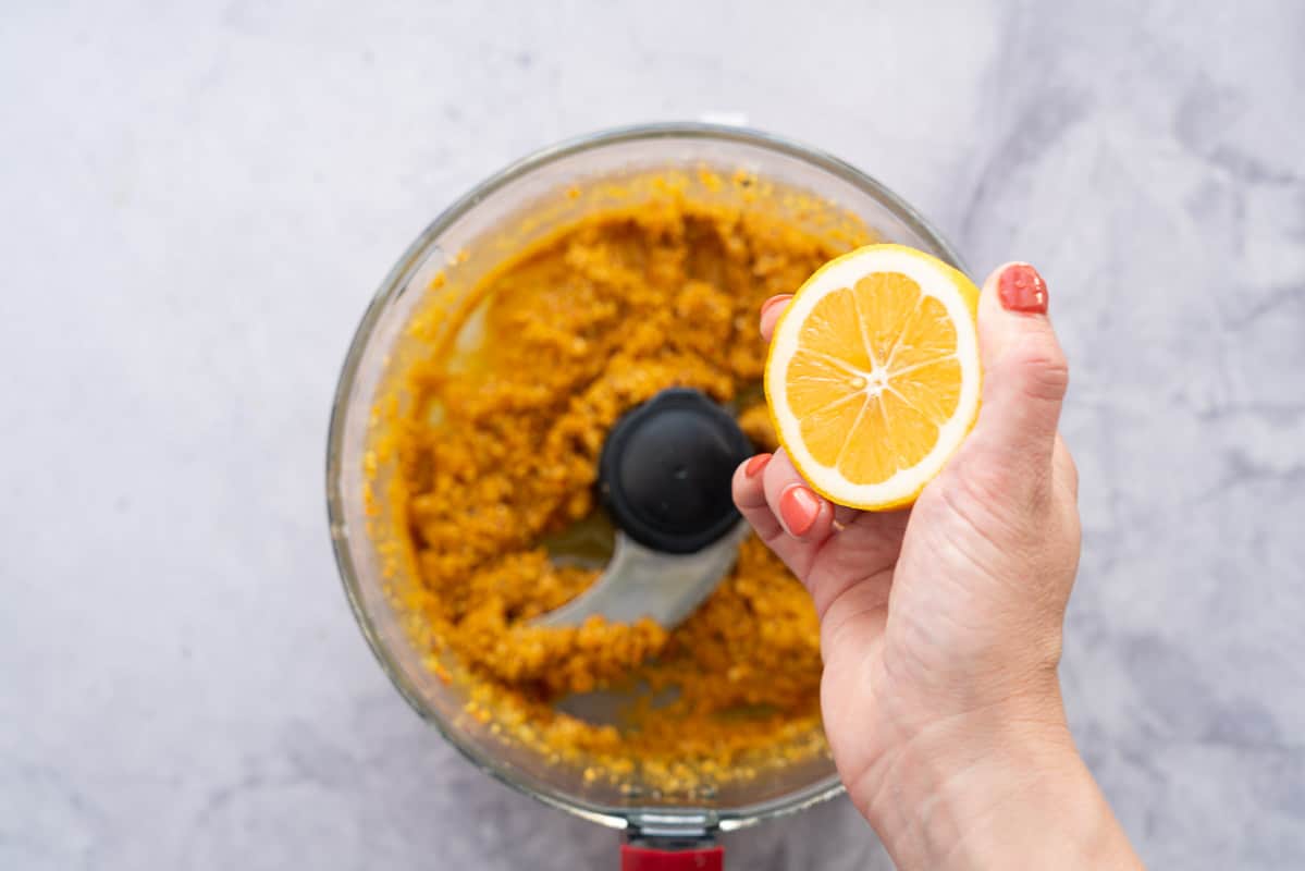 A halved lemon being held above a food processor of carrot pesto.