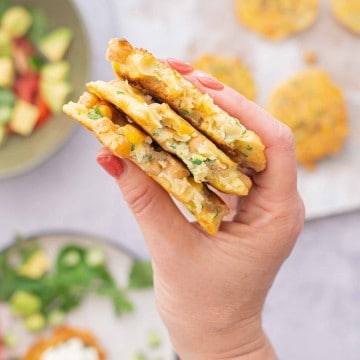 A hand holding a stack of three fritters that have had a mouthful taken from them to reveal chickpeas, corn and zucchini inside.