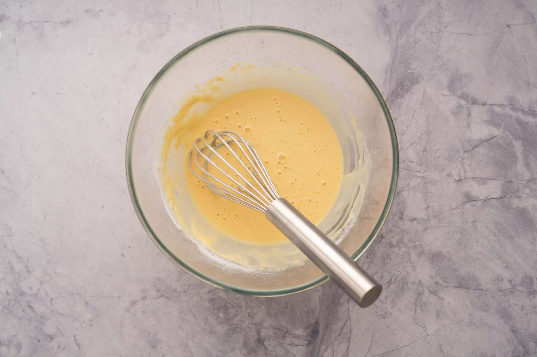 Mixed fritter batter in a large mixing bowl with a whisk sitting on the bench