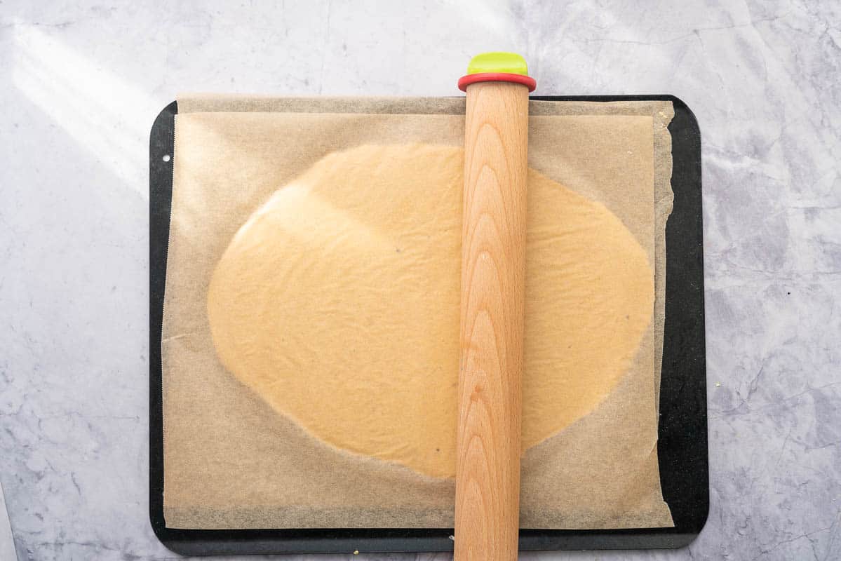 Dough sandwiched between 2 pieces of baking paper on a baking sheet. 