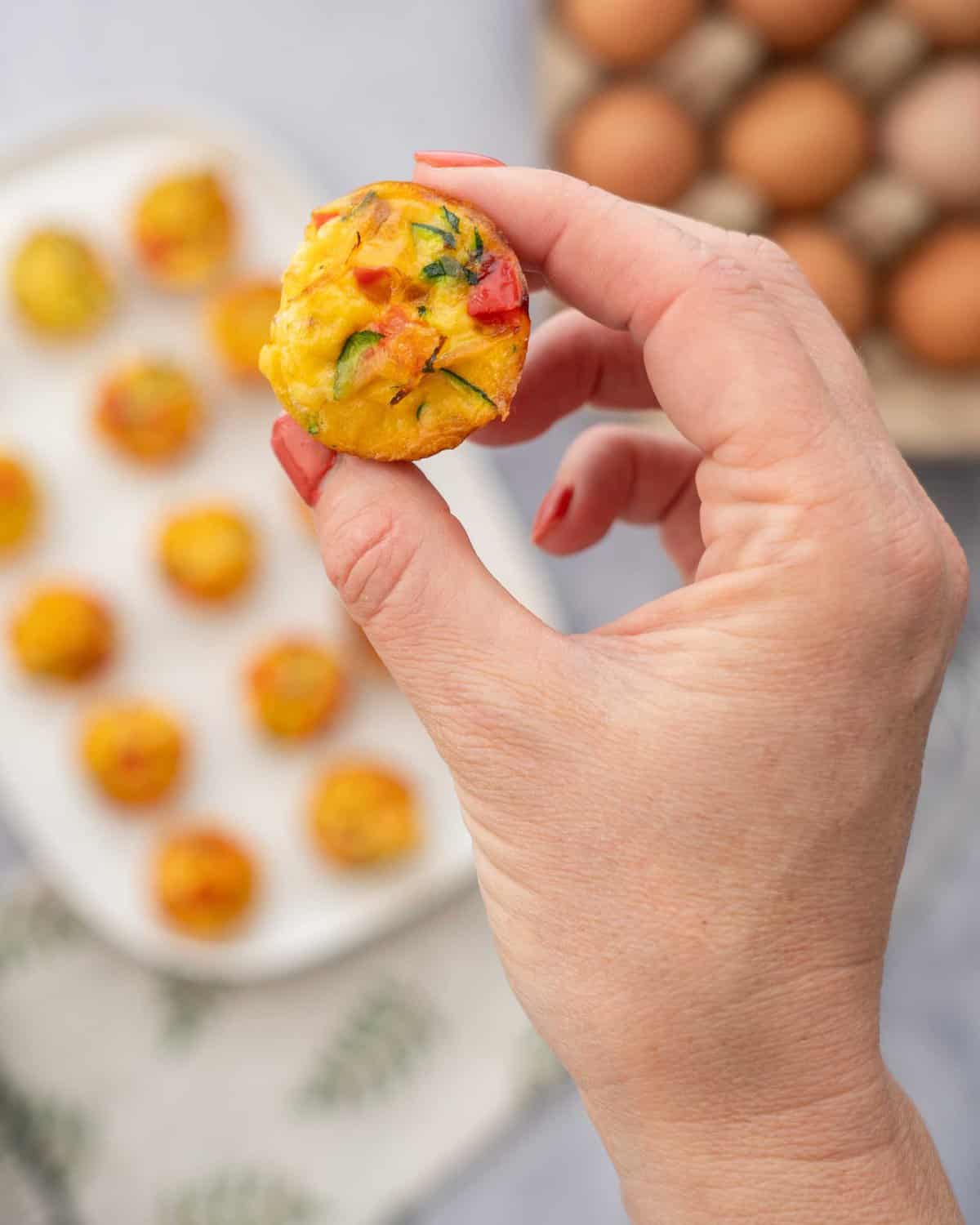 A mini egg muffin studded with colourful vegetables being held up to the camera