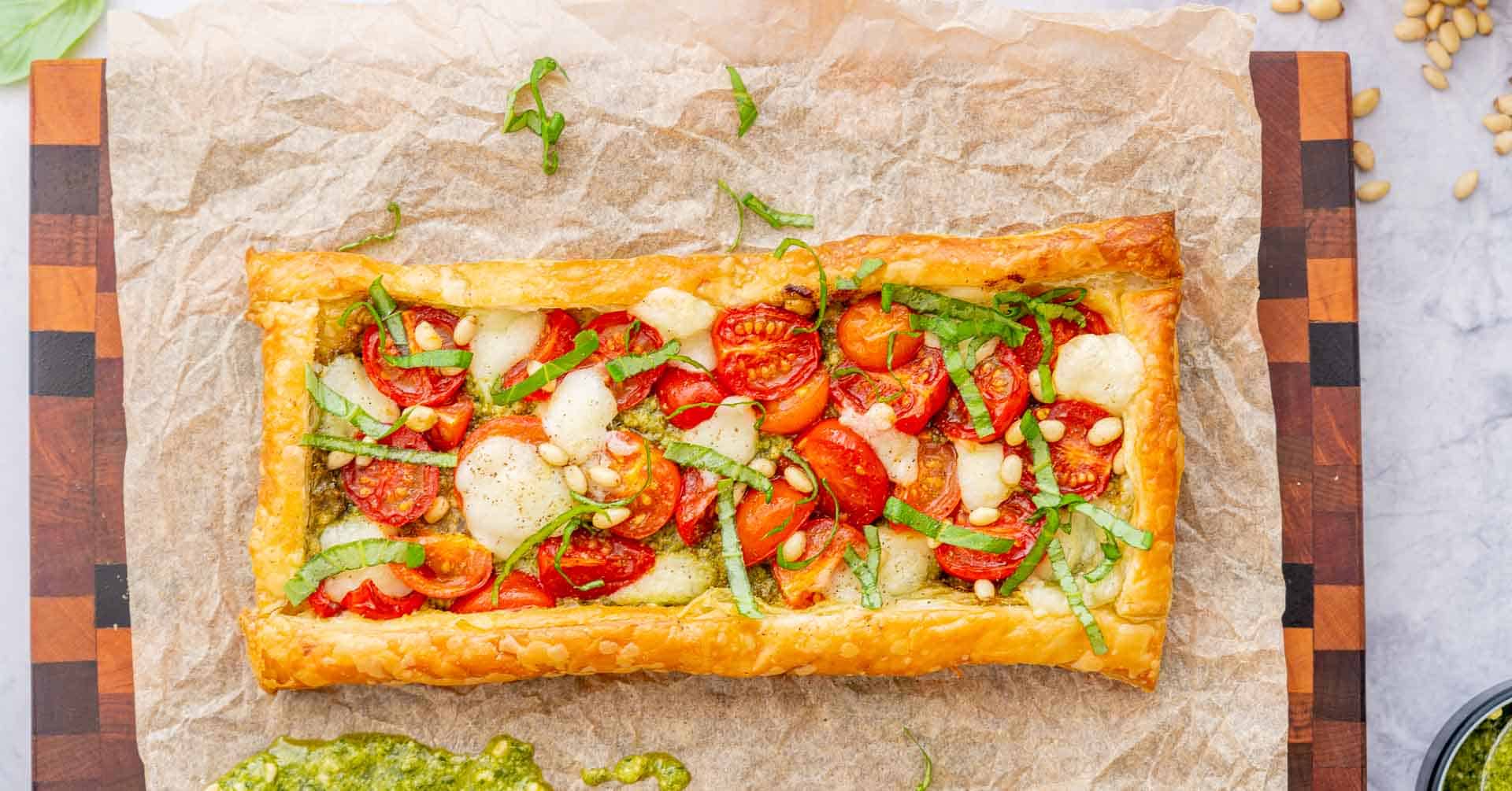 One baked Tomato Tart with sliced basil scattered on the top resting on a chopping board sitting on the bench.
