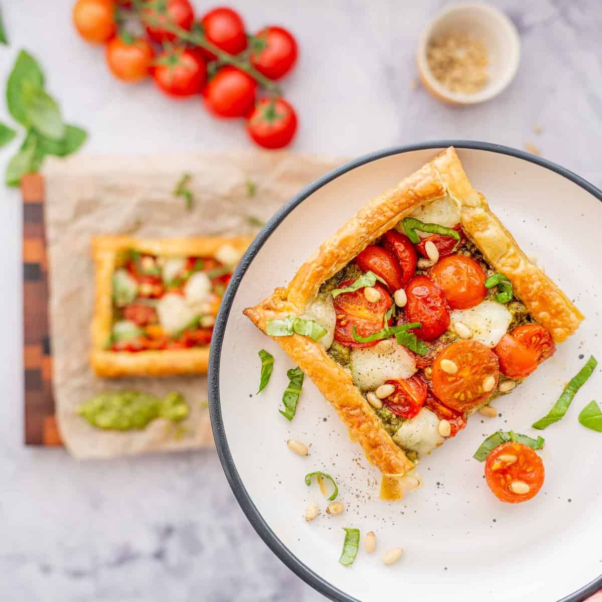 One slice of Tomato tart on a plate raised above the bench  full of ingredients below.