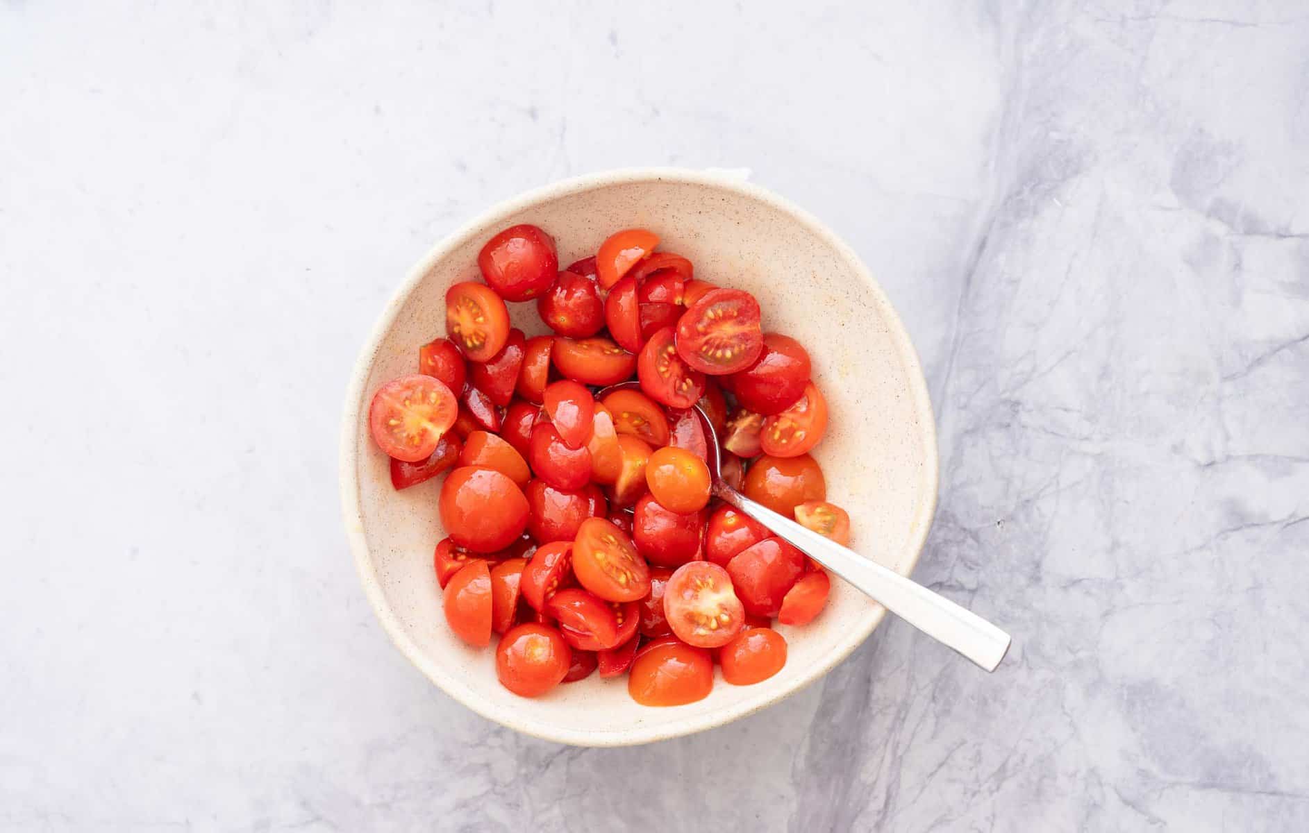 A bowl full of chopped up tomatoes sitting on a bench with a spoon resting in it.