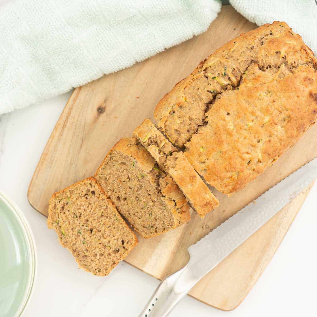 A loaf od banana bread on a wooden chopping board that has been sliced with a stainless steel bread knife. 