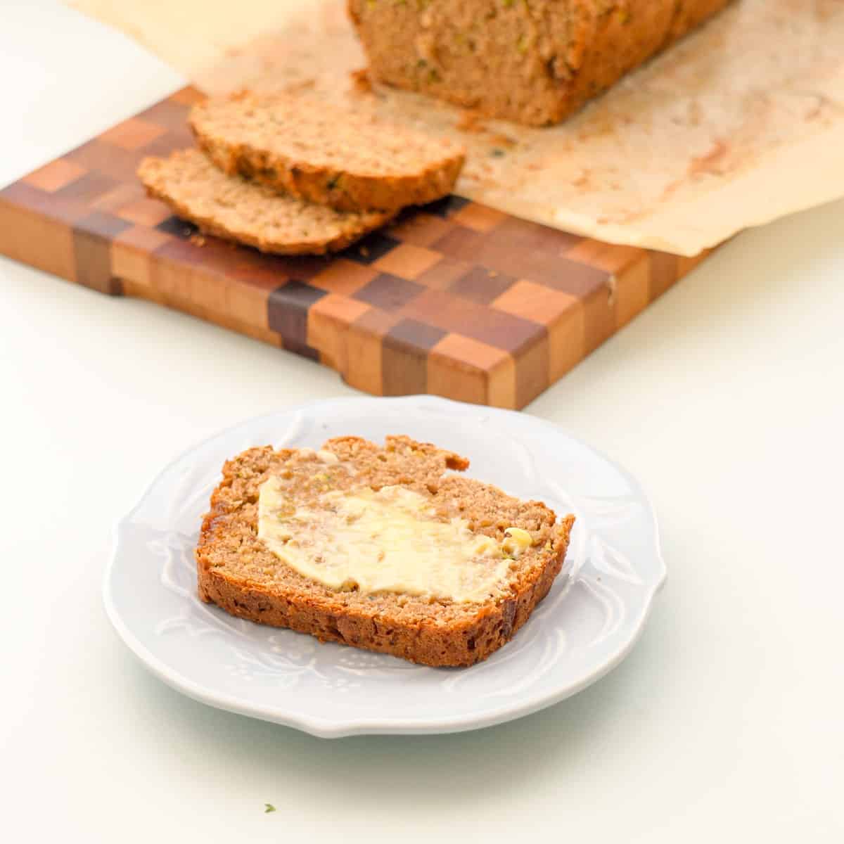 A slice of banana bread spread with butter on a patterned side plate. 
