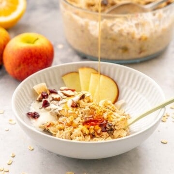 A bowl of bircher muesli, sliced apple and yoghurt being drizzled with honey.