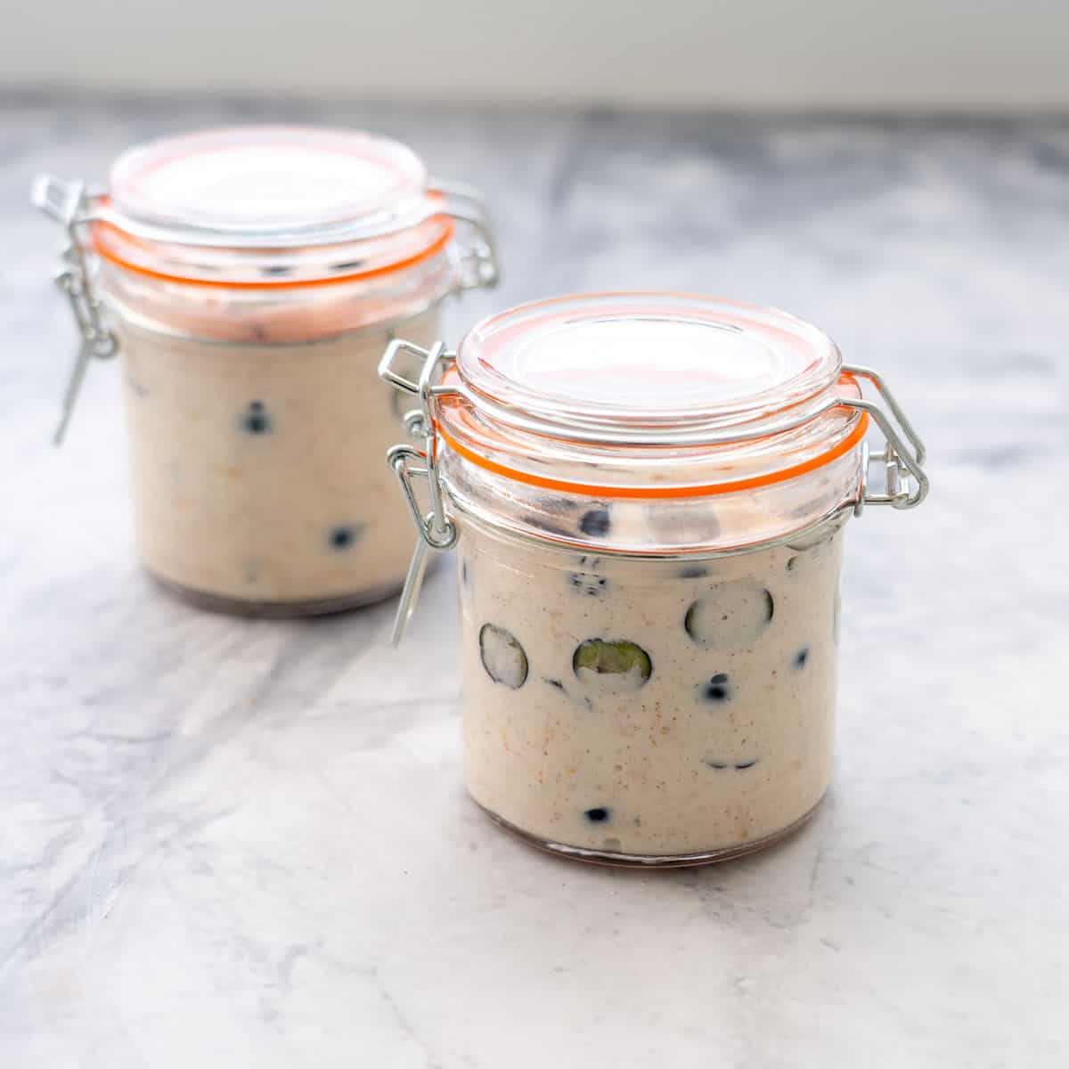 Two portioned jars filled with the Blueberry overnight oats sitting on the bench