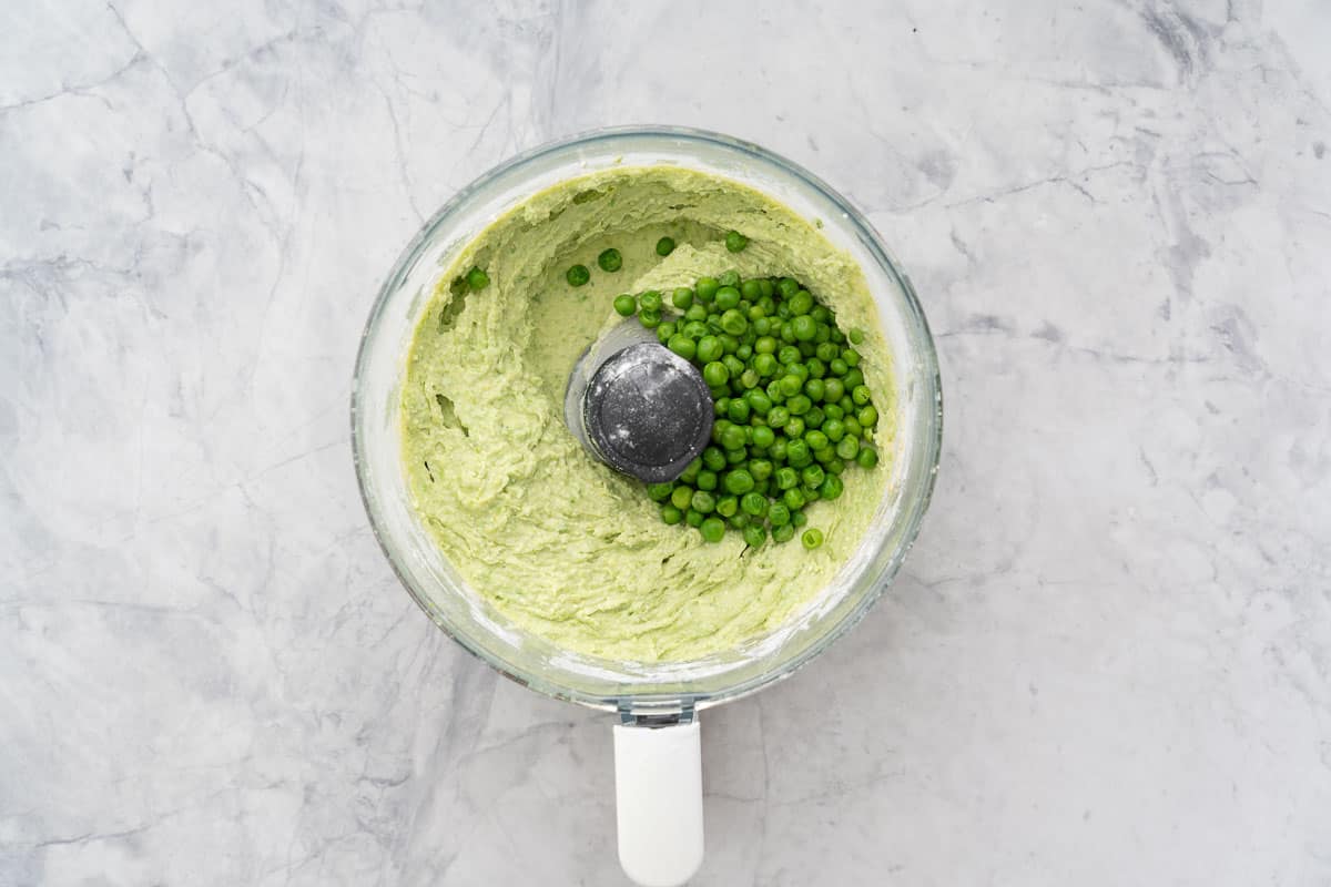 Whizzed ingredients with the second measure of peas added to the food processor which is sitting on the bench