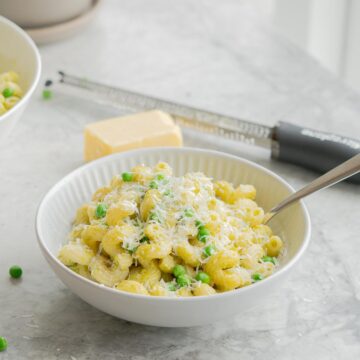 A bowl of spiral pasta with peas visible and parmesan cheese.