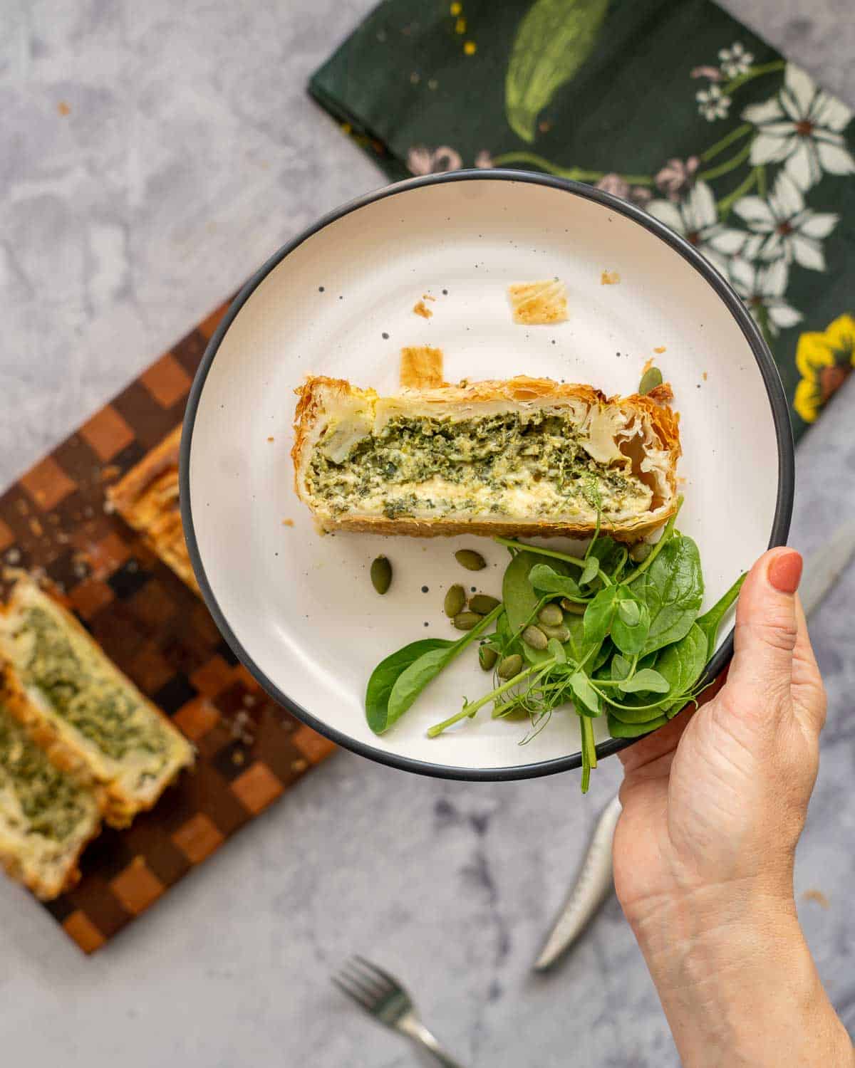 A plate with a slice of spinach cheese pie  being held up to the camera. 