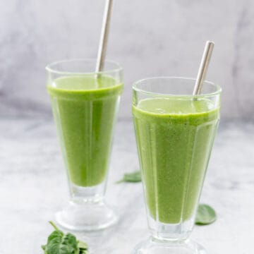 Two glasses with stainless steel straws filled with green smoothie.