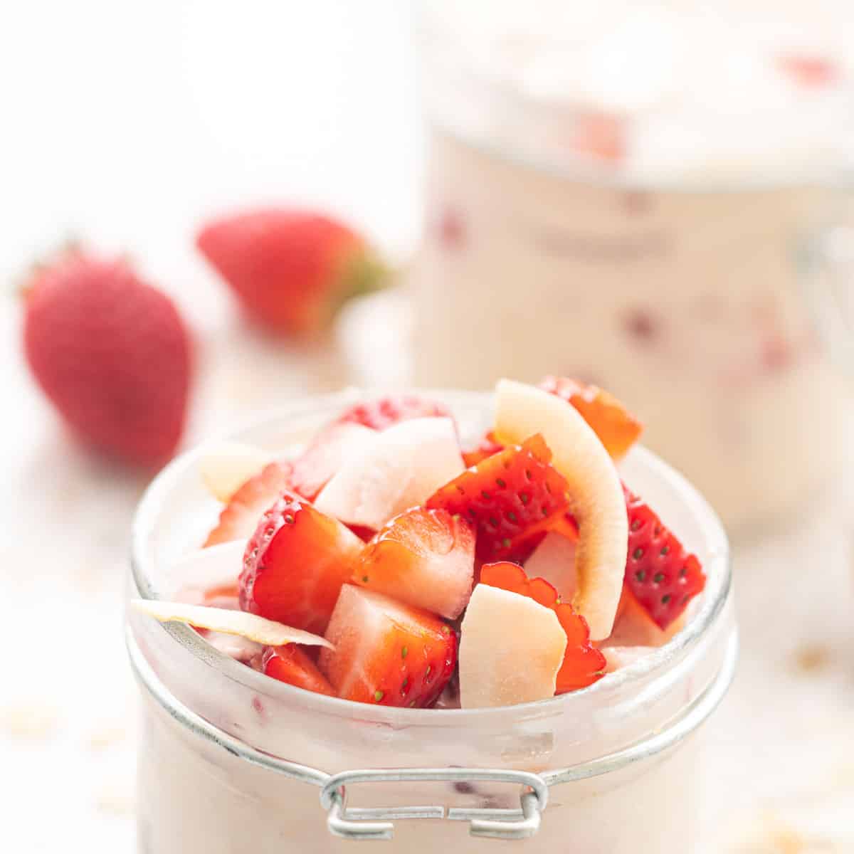 Chopped strawberries and coconut flakes resting on the top of a jar of overnight oats. 