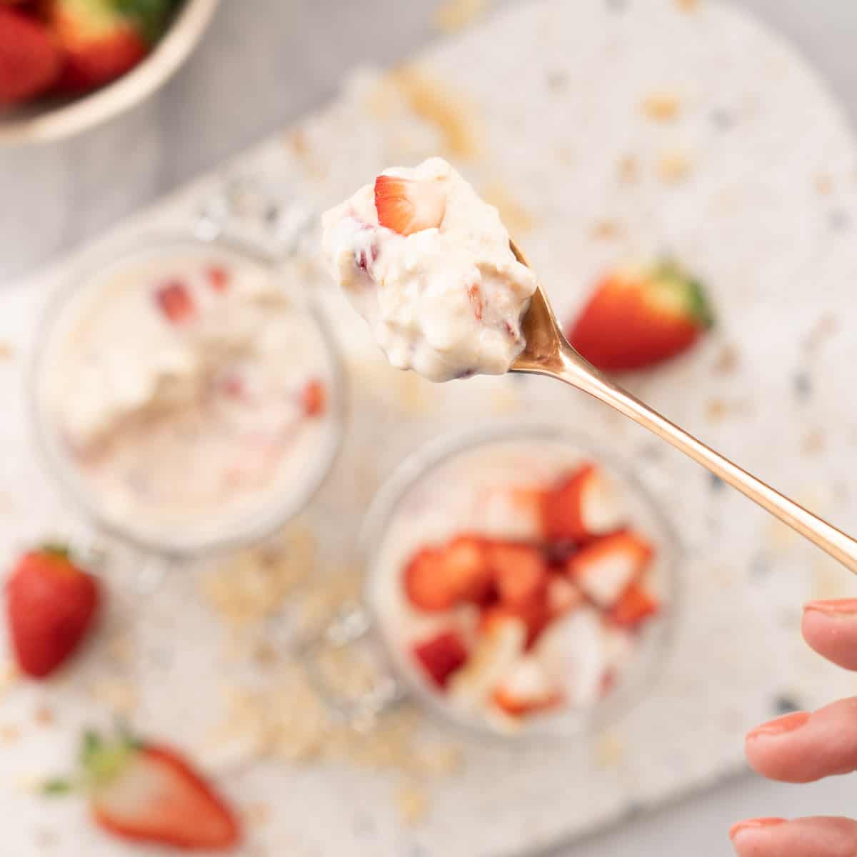 A spoonful of strawberry overnight oats being held up to the camera, creamy oats and chunks of strawberry visible/