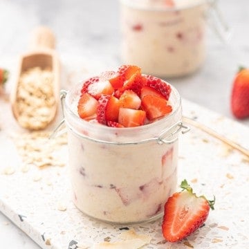 A glass jar filled with creamy oats topped with diced pieces of red strawberry.