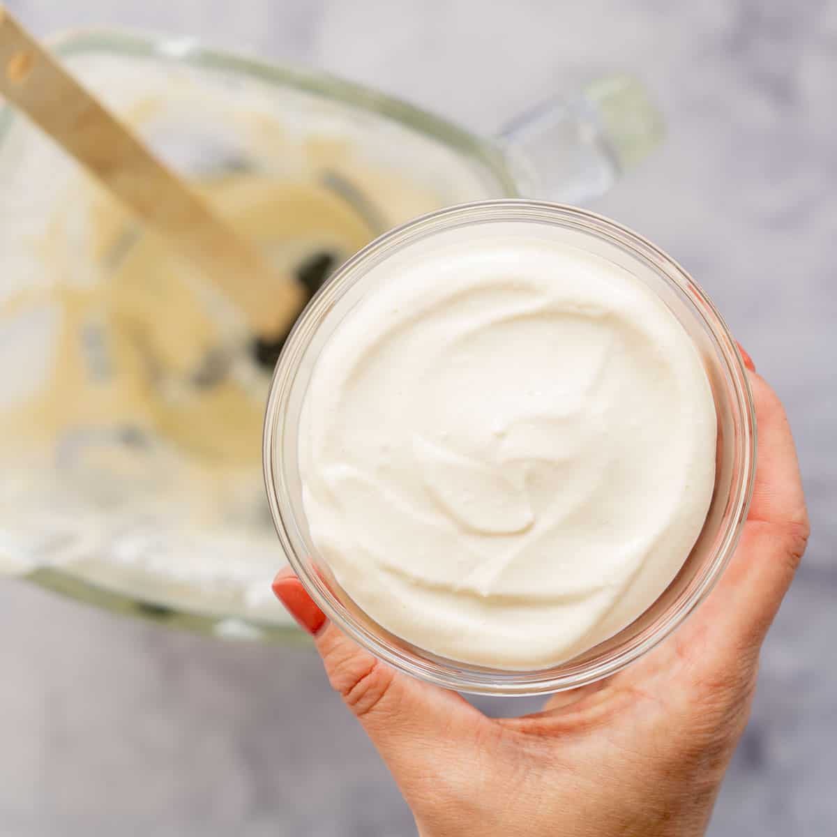 A hand holding up a glass bowl of Whipped Cottage Cheese dip above the blender