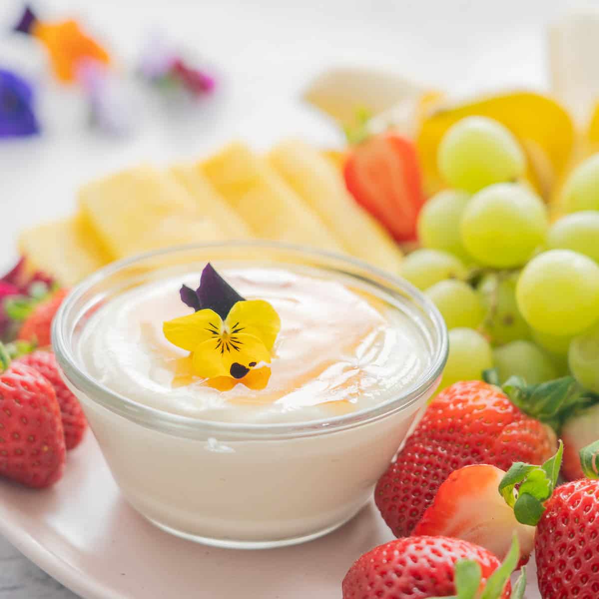 A plate full of fresh strawberries, grapes, bananas and pineapple and the Whipped cottage cheese dip in a glass ramekin 