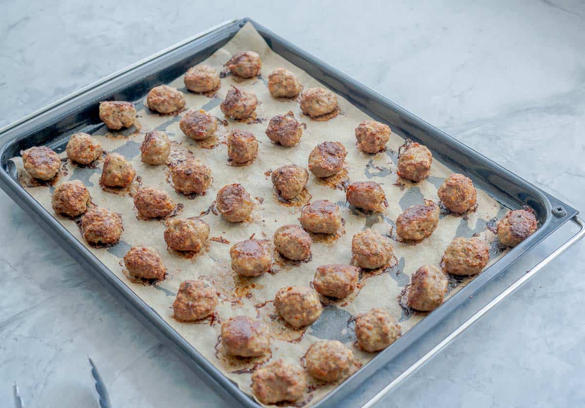 Baked meatballs laid out on a linebacking tray that is sitting on a bench 