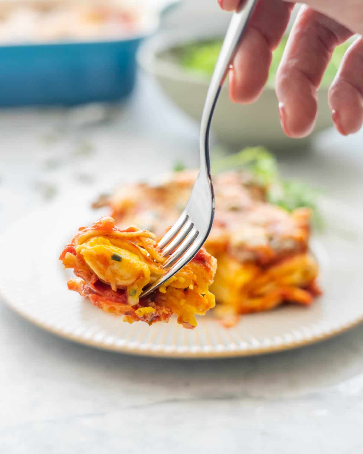 A serving of Butternut Squash Pasta and a side salad on a plate with forkful held above it.  