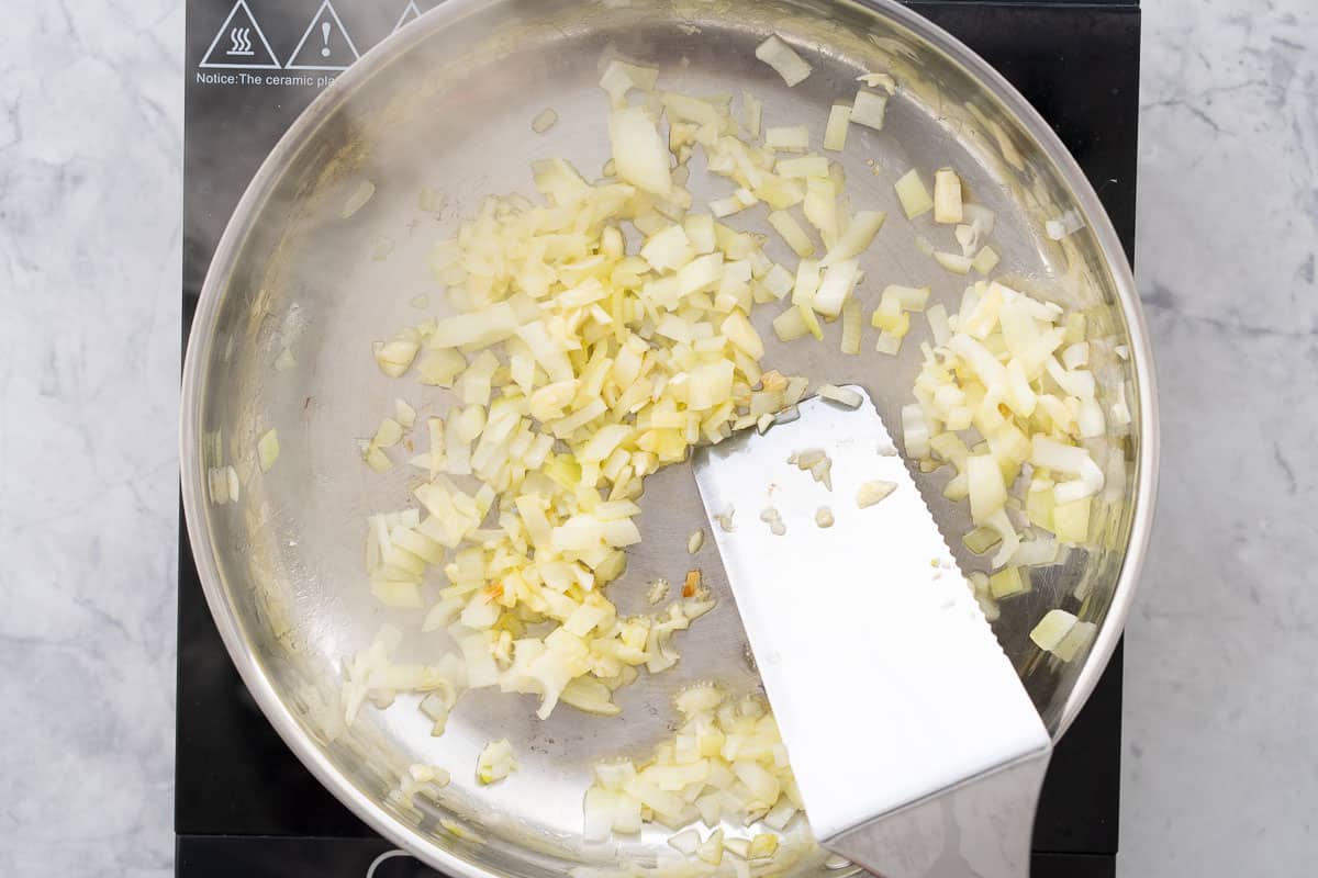 Diced onions and garlic sautéing in a frying pan on a bench top element.