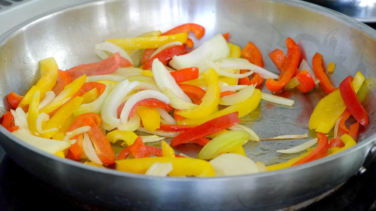 Sliced capsicum and onions salting in an oiled frying pan 