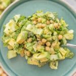 A salad made with chickpeas and avocados on a turquoise plate being held up above a large bowl of salad.