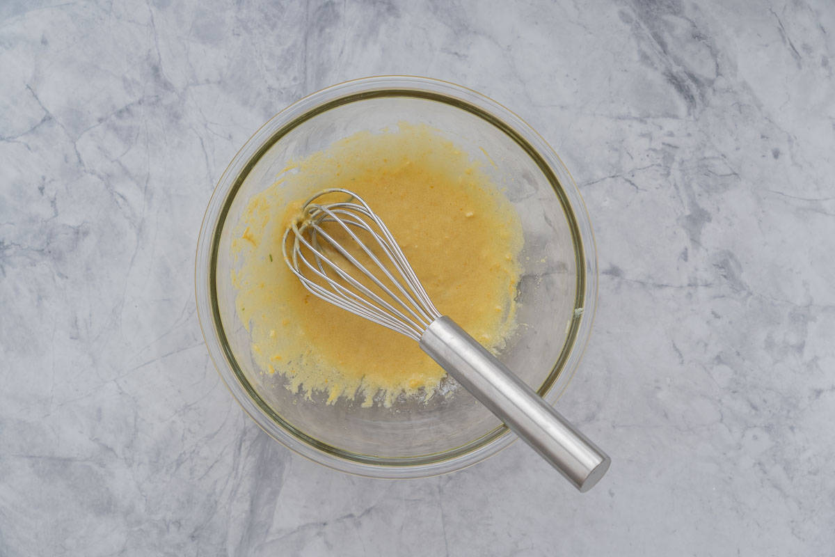 A large glass mixing bowl with a creamy mustard salad dressing whisked in the bottom of it. 