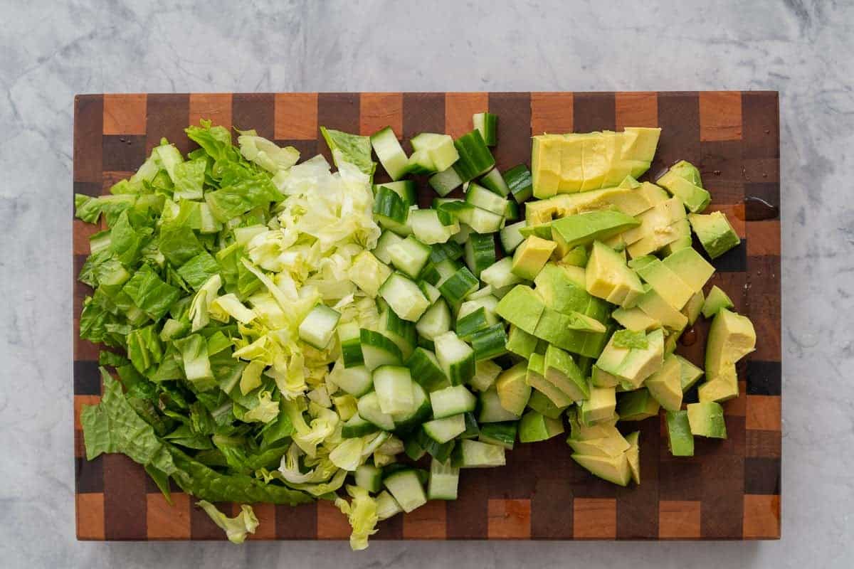 Chopped lettuce, cucumber and avocado on a wooden chopping board. 