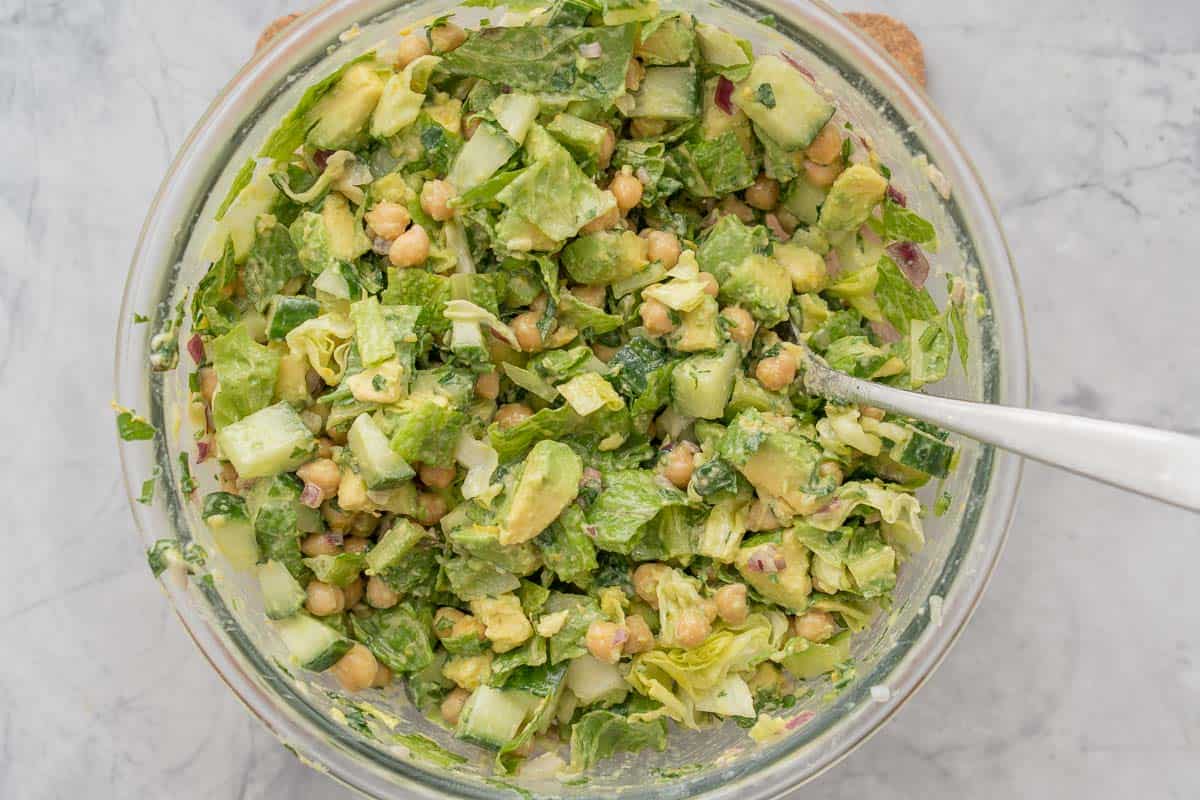 Chickpea and avocado salad tossed in a large glass mixing bowl. 