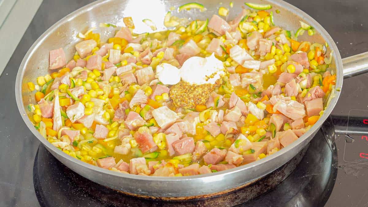 Sautéing onions, zucchini, carrots, corn kernals and ham in a frying pan on a induction element with mustard and sour cream added