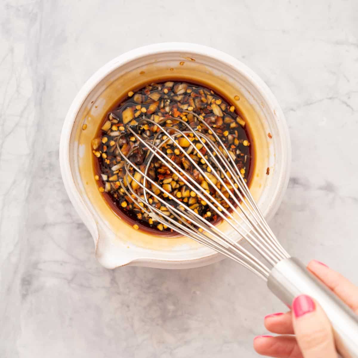 honey, soy, lemon juice and garlic being whisked together in a bowl which is sitting on the bench 