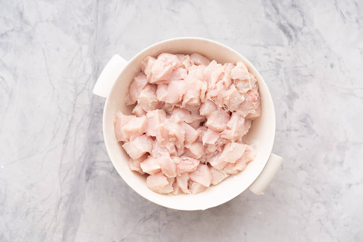 A large bowl of diced chicken sitting on the bench 