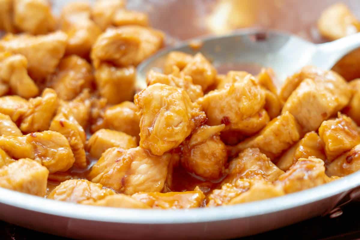 Honey garlic chicken pieces in a pan with a serving spoon resting on the side 