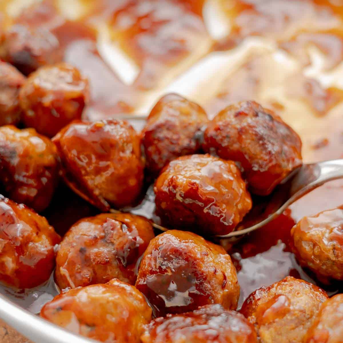A spoonful of baked meatballs in a soy honey glaze sauce slightly raised above the rest of the batch. 