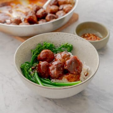 A bowl with meatballs in a sticky sauce, steamed brococlini and rice.