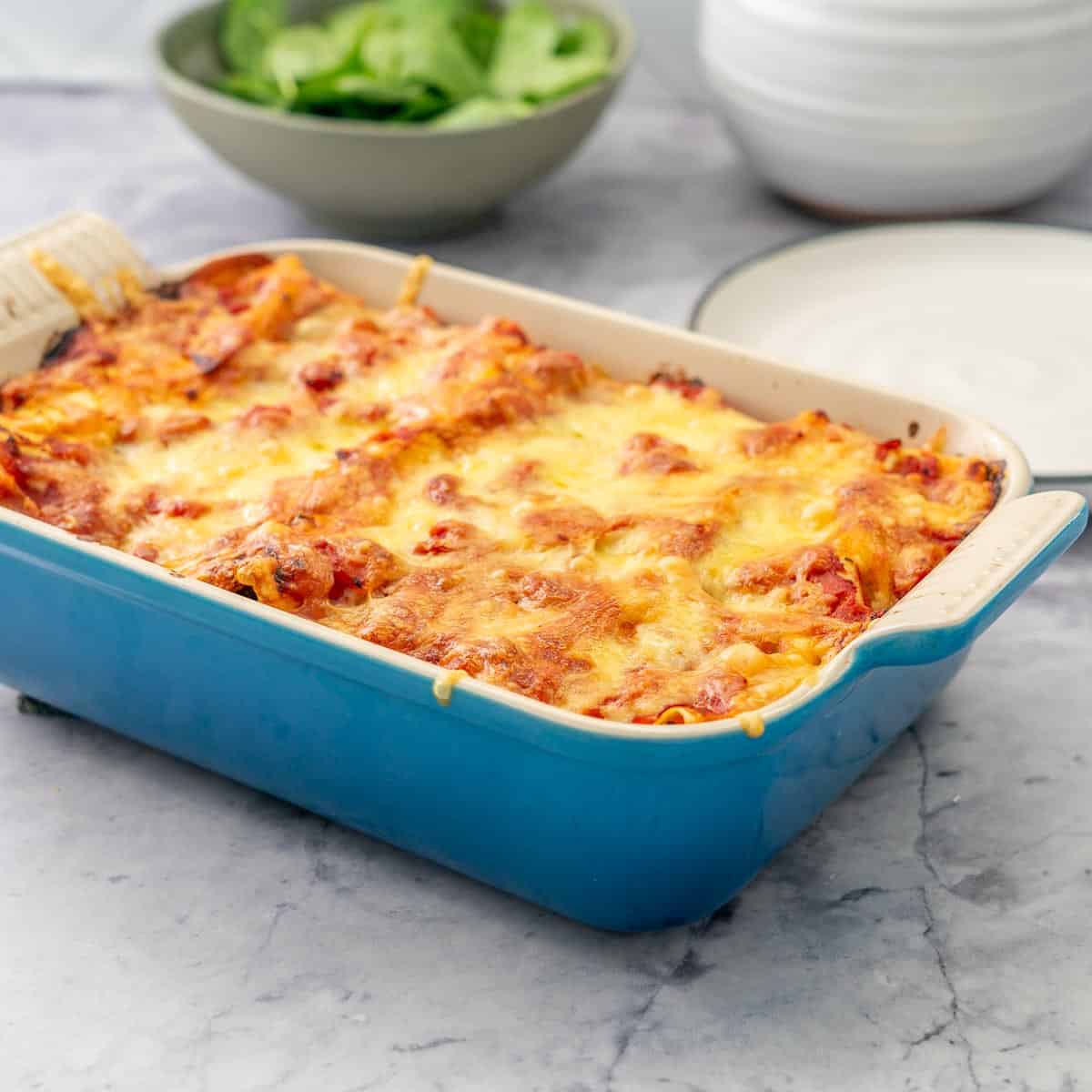 Baked Lasagna roll ups in a blue oven dish sitting on the bench with a green salad in the background 