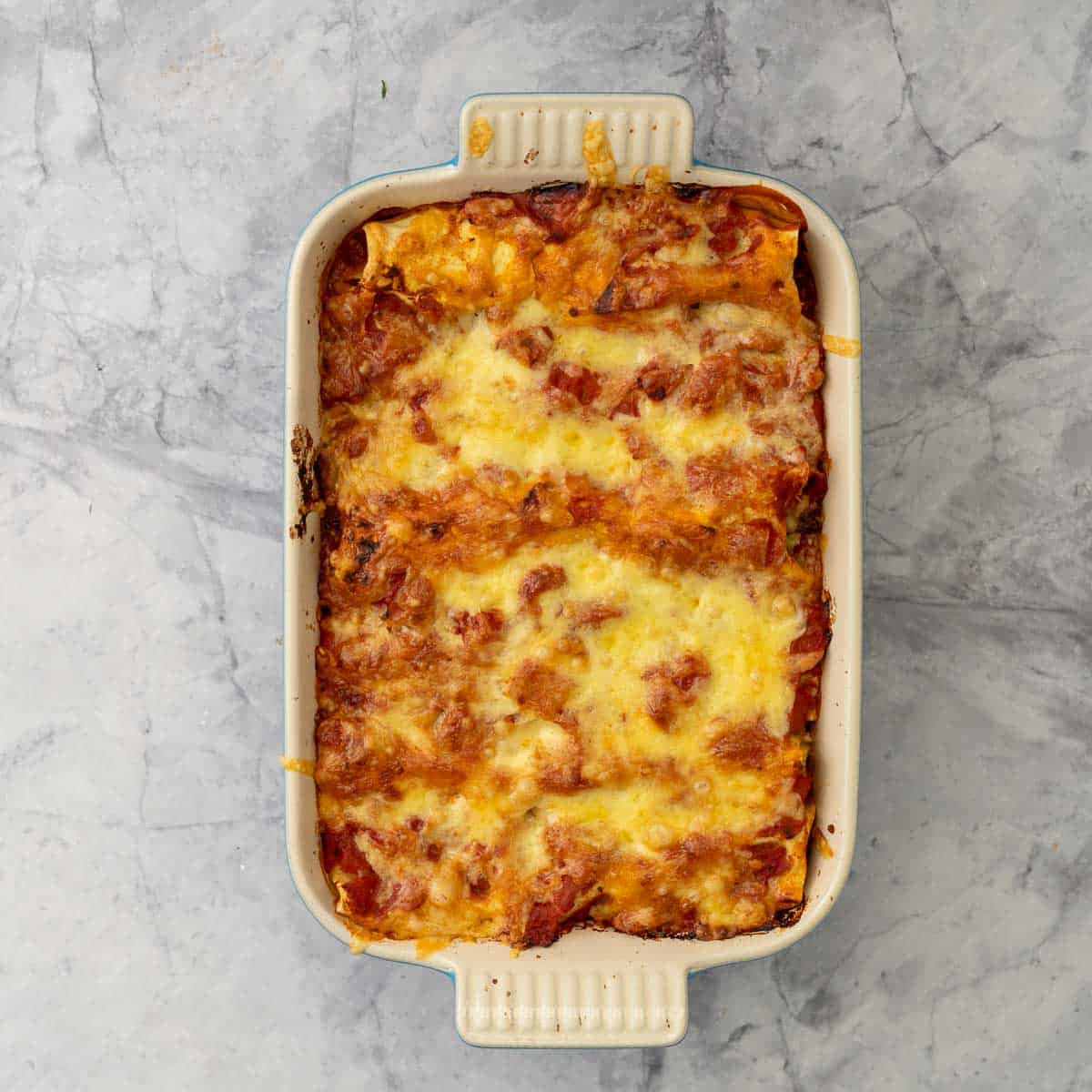Baked Lasagna roll ups in a oven dish sitting on the bench. 