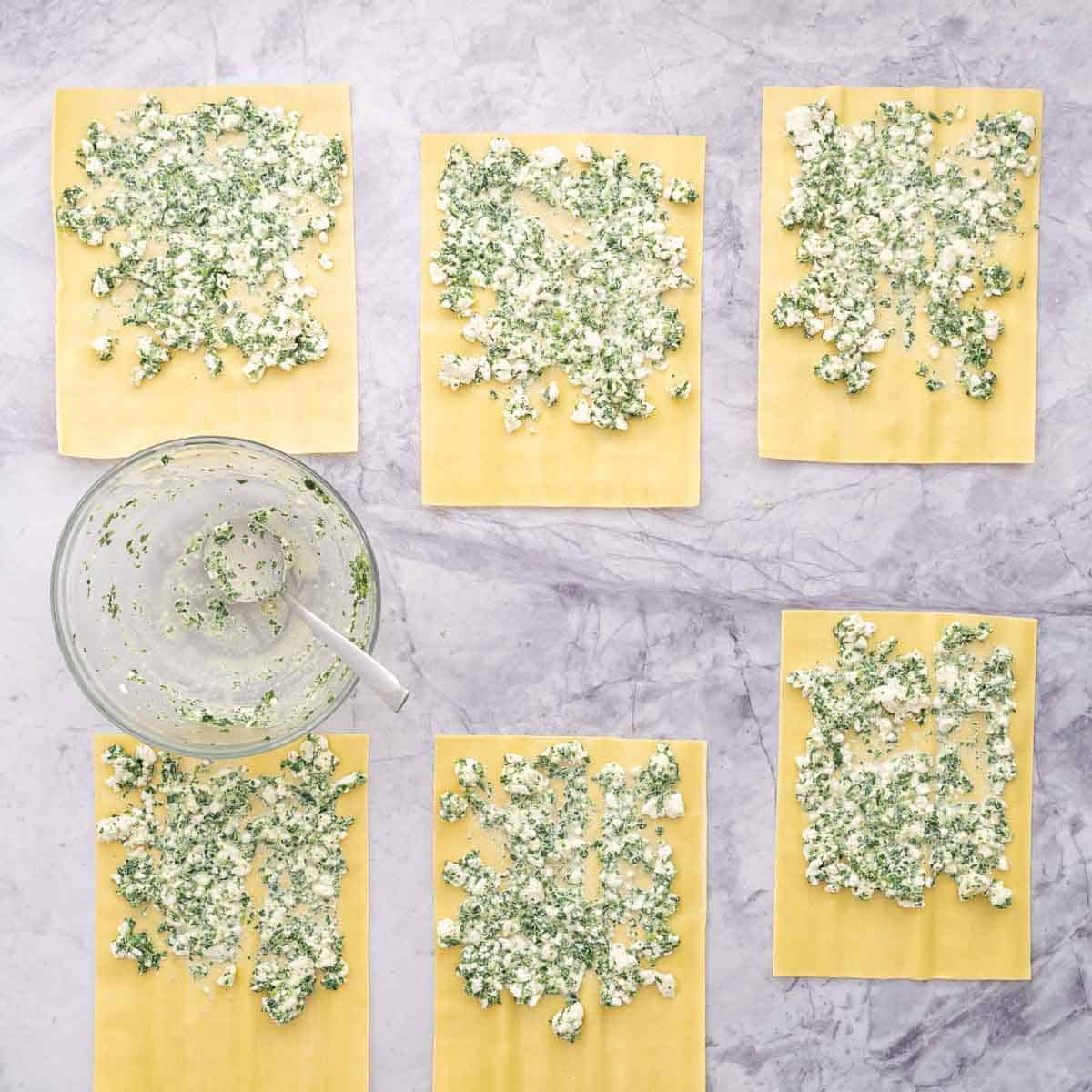 Fresh lasagne sheets laid out on the bench with each sheet spread with a layer of spinach and cottage cheese mixture.
