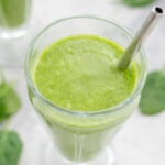 One glass of spinach smoothie placed on the bench with a straw and a scattering of spinach leaves.