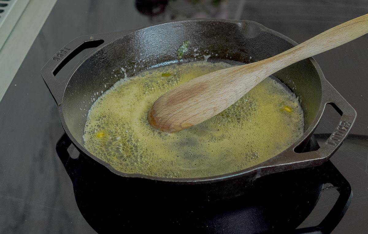 A cast iron pan with melted butter bubbling away in it with a wooden spoon resting on the side. 