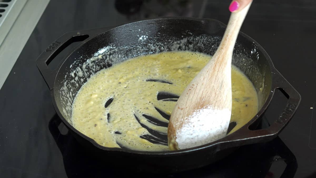 Flour being stirred into the cast iron pan of melted butter by a wooden spoon.